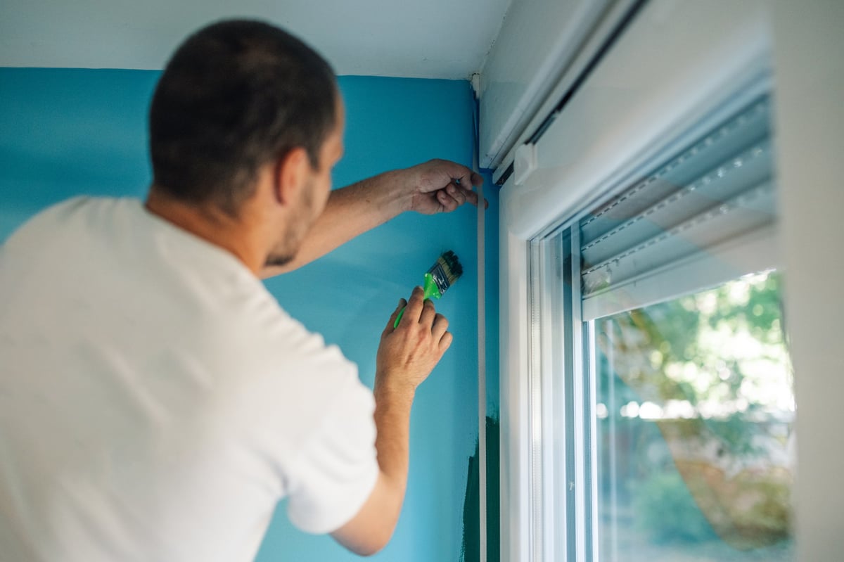 Painter taping off a window frame before painting an interior wall
