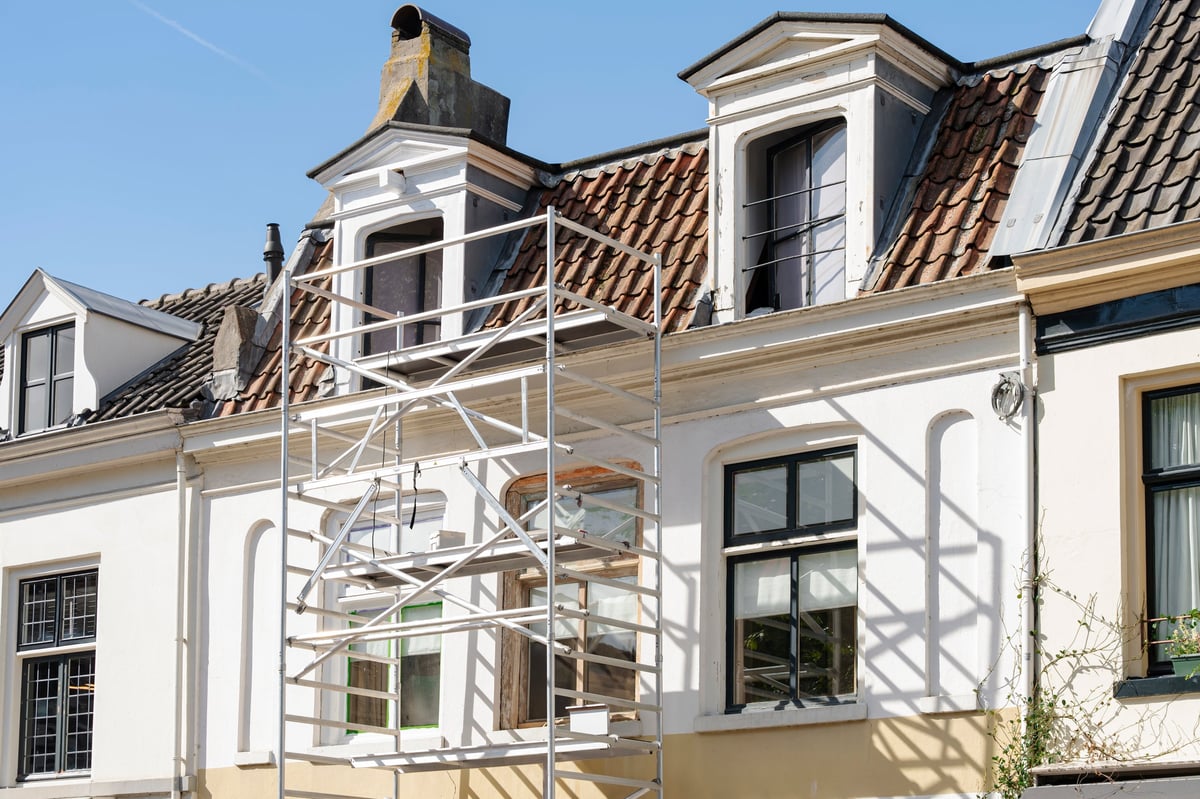 Scaffolding against a white house with a red tile roof during maintenance work